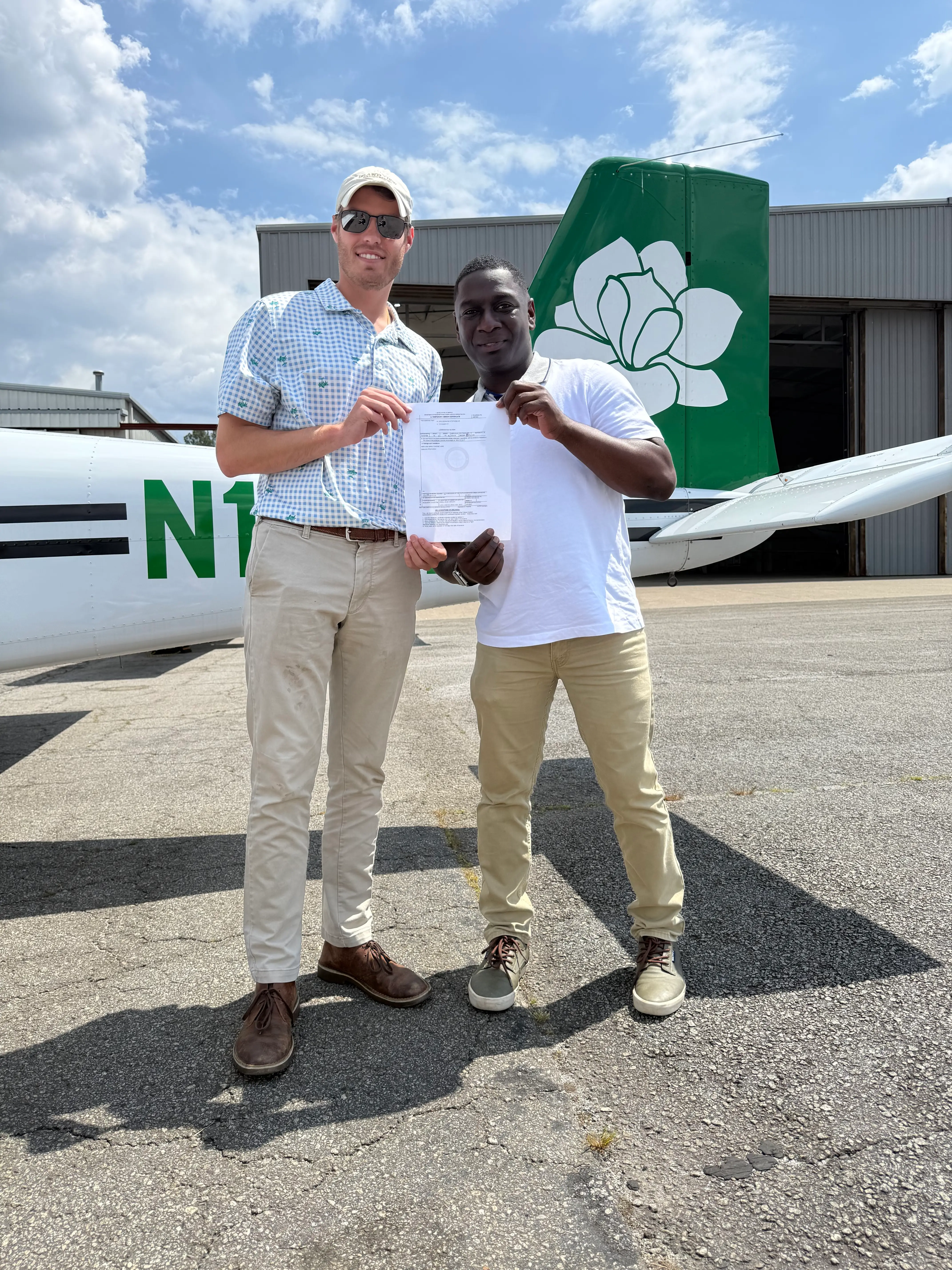 Magnolia Aviation Academy male CFI with male student holding certificate in front of aircraft